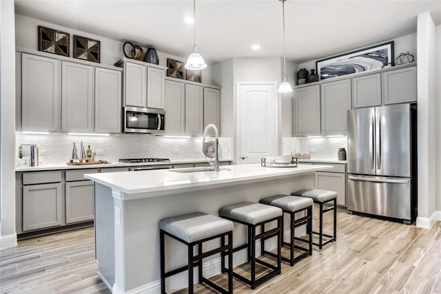 kitchen featuring gray cabinetry, stainless steel appliances, sink, hanging light fixtures, and a center island with sink