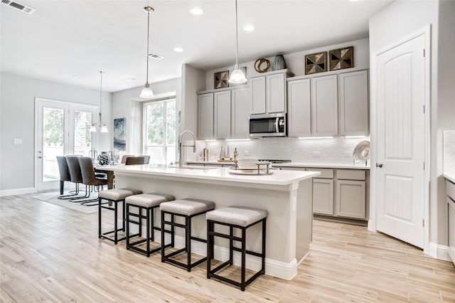 kitchen with gray cabinets, hanging light fixtures, and a center island with sink