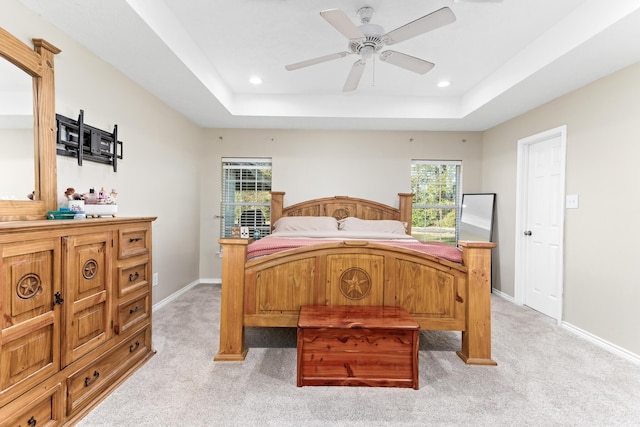 bedroom with ceiling fan, light colored carpet, and a tray ceiling