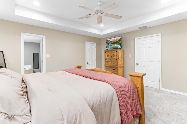 bedroom featuring ceiling fan, ensuite bathroom, a raised ceiling, and carpet