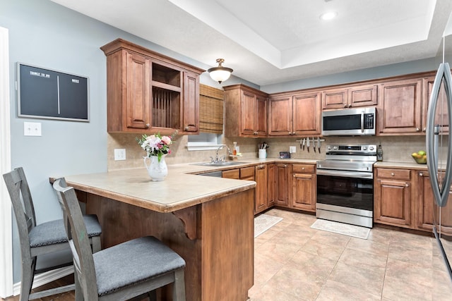 kitchen with kitchen peninsula, a kitchen breakfast bar, sink, decorative backsplash, and stainless steel appliances