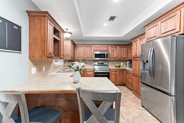 kitchen featuring kitchen peninsula, sink, a tray ceiling, a breakfast bar area, and stainless steel appliances