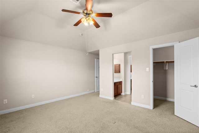 unfurnished bedroom featuring a walk in closet, lofted ceiling, connected bathroom, ceiling fan, and light colored carpet