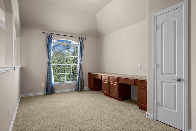 carpeted home office with lofted ceiling and built in desk