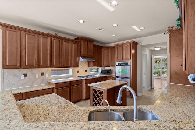 kitchen with appliances with stainless steel finishes, a center island, tasteful backsplash, sink, and light stone counters