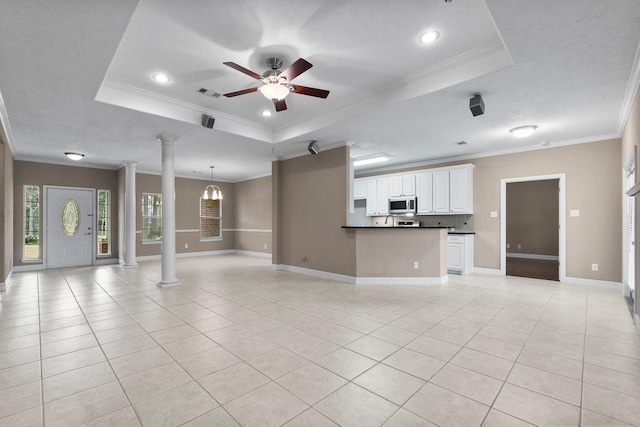 unfurnished living room with crown molding, a raised ceiling, and decorative columns