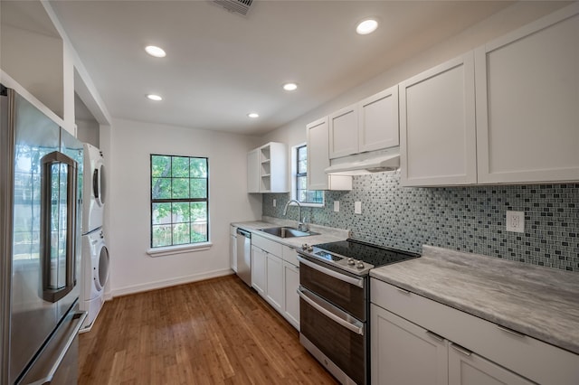 kitchen featuring sink, white cabinetry, stacked washer / dryer, light hardwood / wood-style floors, and stainless steel appliances