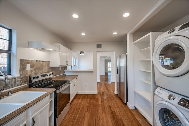 kitchen featuring exhaust hood, white cabinets, stacked washer and clothes dryer, and appliances with stainless steel finishes