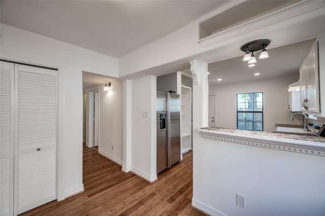 kitchen with hardwood / wood-style flooring, stainless steel refrigerator with ice dispenser, white cabinetry, and sink