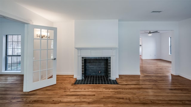 unfurnished living room featuring ceiling fan, dark hardwood / wood-style floors, and a tiled fireplace