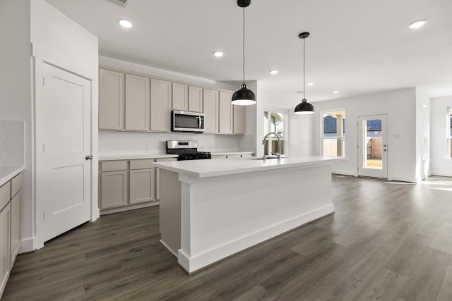 kitchen with sink, an island with sink, hanging light fixtures, and appliances with stainless steel finishes