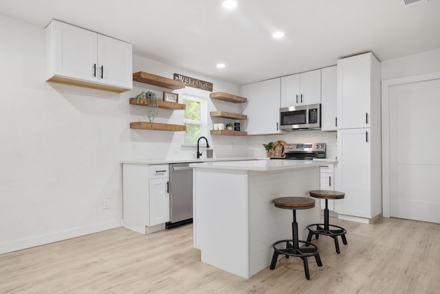 kitchen with light hardwood / wood-style floors, a breakfast bar, white cabinetry, and appliances with stainless steel finishes