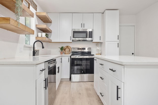 kitchen with appliances with stainless steel finishes, white cabinetry, sink, light stone counters, and light hardwood / wood-style flooring