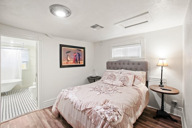 bedroom with a textured ceiling, dark hardwood / wood-style floors, and ensuite bath