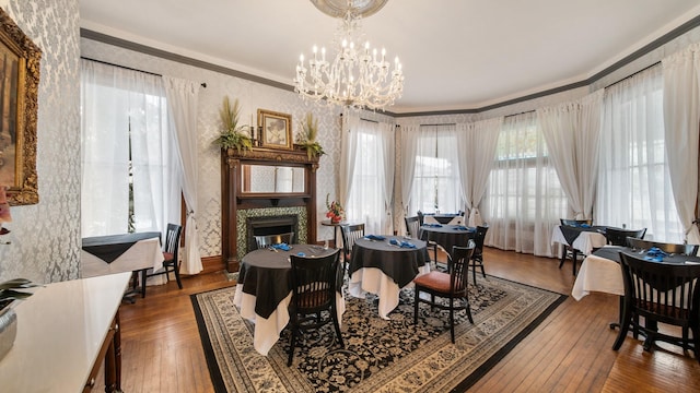 dining area with wood-type flooring, a tiled fireplace, an inviting chandelier, and ornamental molding