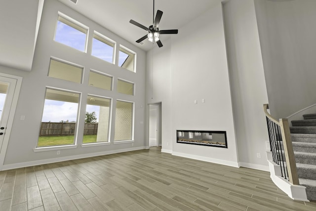 10807 Lighthouse Peak Trce, Richmond, TX 77406 - unfurnished living room featuring a towering ceiling, a ceiling fan, wood finished floors, stairway, and baseboards