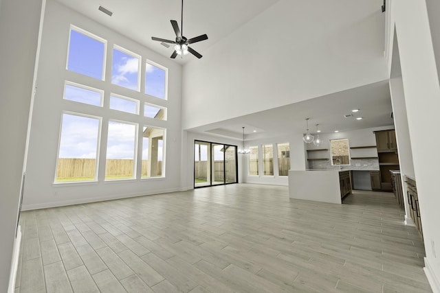26515 Castra Crescent Trl, Richmond, TX 77406 - unfurnished living room with a ceiling fan, a high ceiling, a chandelier, light wood-type flooring, and baseboards