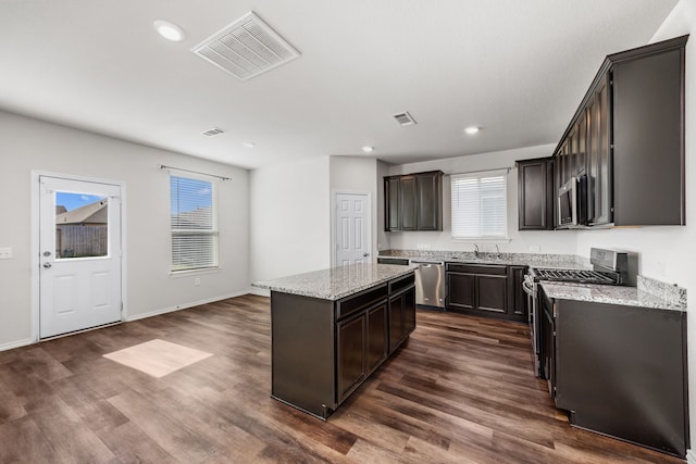 kitchen with stainless steel appliances, a center island, a healthy amount of sunlight, and light stone countertops