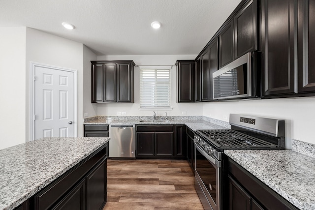 kitchen with light stone countertops, dark wood-type flooring, appliances with stainless steel finishes, and sink