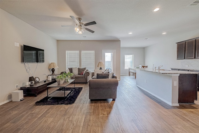 living room with light hardwood / wood-style floors, a textured ceiling, and ceiling fan