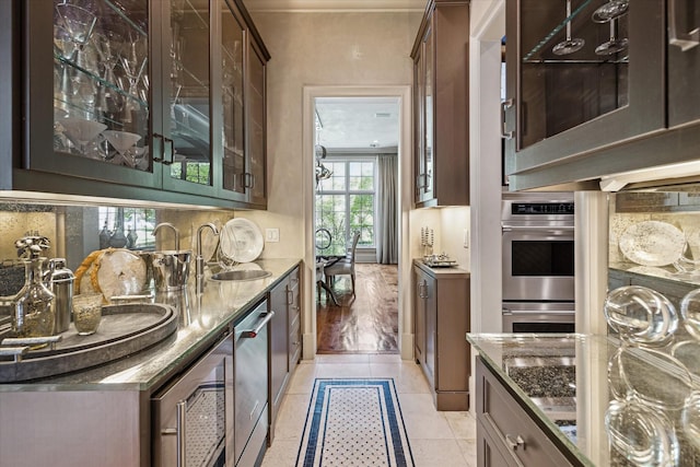 bar featuring sink, light tile patterned floors, stainless steel appliances, and dark stone counters