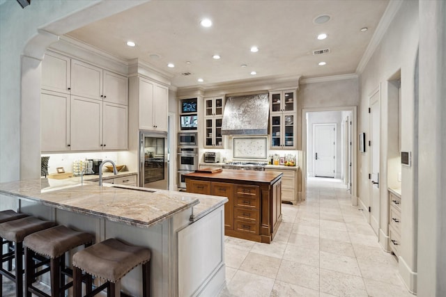 kitchen with sink, kitchen peninsula, light stone counters, a breakfast bar, and custom range hood