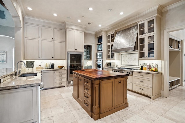 kitchen with a center island, custom exhaust hood, sink, backsplash, and butcher block countertops