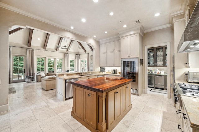 kitchen featuring stainless steel dishwasher, white cabinets, a center island, vaulted ceiling with beams, and wood counters