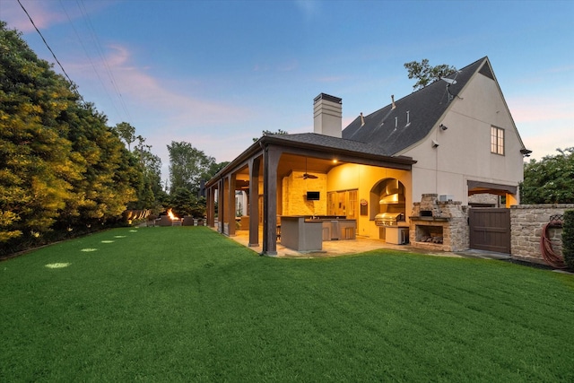 back house at dusk featuring ceiling fan, a patio area, a lawn, and area for grilling