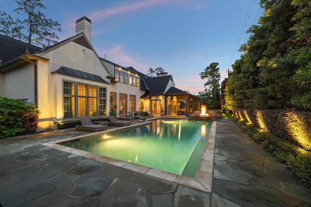 pool at dusk with a patio area and a fire pit