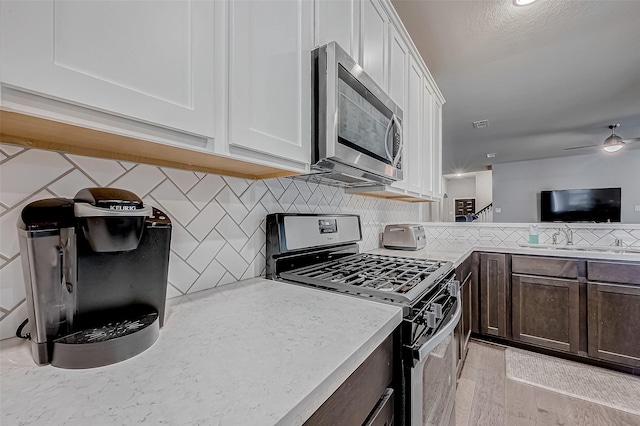 kitchen featuring decorative backsplash, white cabinets, dark brown cabinetry, light wood-type flooring, and stainless steel appliances