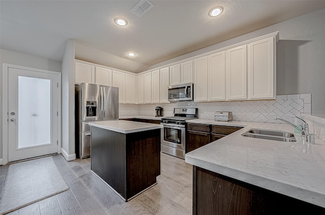 kitchen featuring a center island, white cabinetry, stainless steel appliances, sink, and light hardwood / wood-style flooring