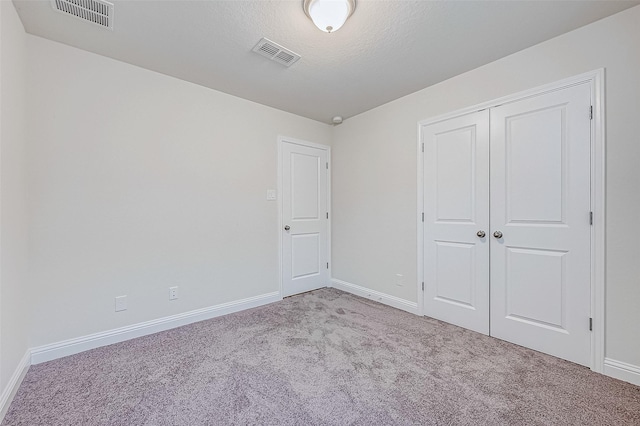 unfurnished bedroom with light carpet, a textured ceiling, and a closet