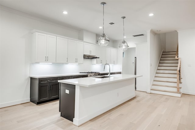 kitchen with decorative light fixtures, sink, white cabinetry, a center island with sink, and decorative backsplash