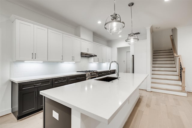 kitchen with high end range, decorative light fixtures, white cabinetry, sink, and a kitchen island with sink