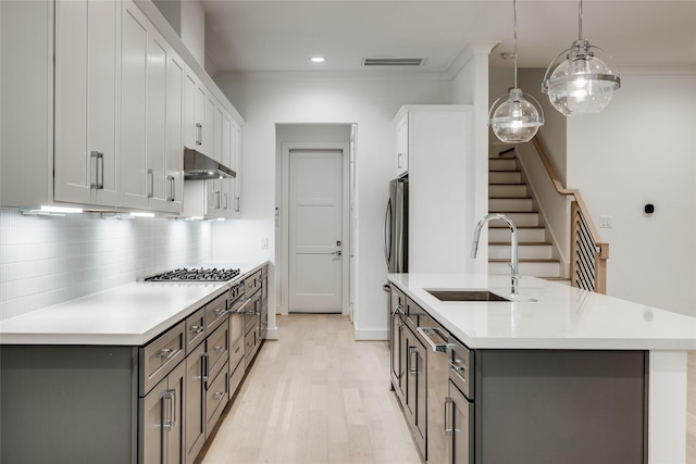 kitchen with hanging light fixtures, sink, white cabinets, ornamental molding, and a center island with sink