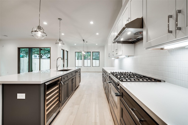 kitchen featuring high end range, sink, white cabinets, a center island with sink, and wine cooler