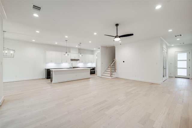 unfurnished living room featuring light hardwood / wood-style floors, sink, crown molding, and ceiling fan