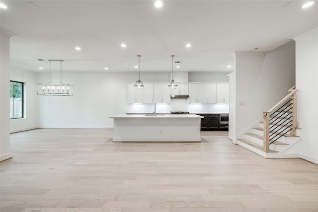 kitchen with decorative light fixtures, sink, white cabinetry, a kitchen island with sink, and light hardwood / wood-style floors