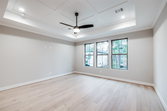 empty room with ceiling fan, a tray ceiling, light hardwood / wood-style flooring, and crown molding