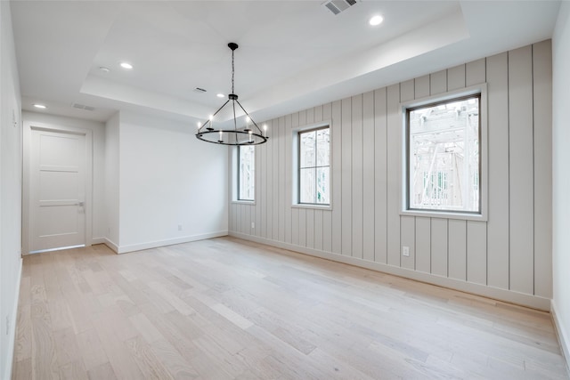 spare room with a raised ceiling, a chandelier, and light wood-type flooring