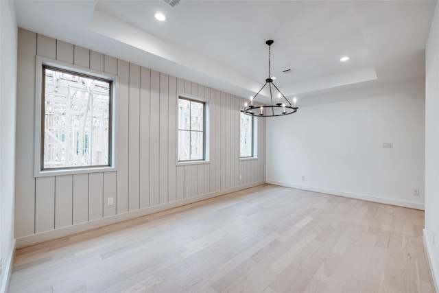 spare room with light wood-type flooring, a tray ceiling, and an inviting chandelier