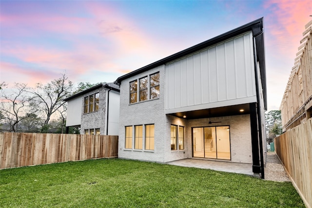 back house at dusk featuring a patio area, a yard, and ceiling fan