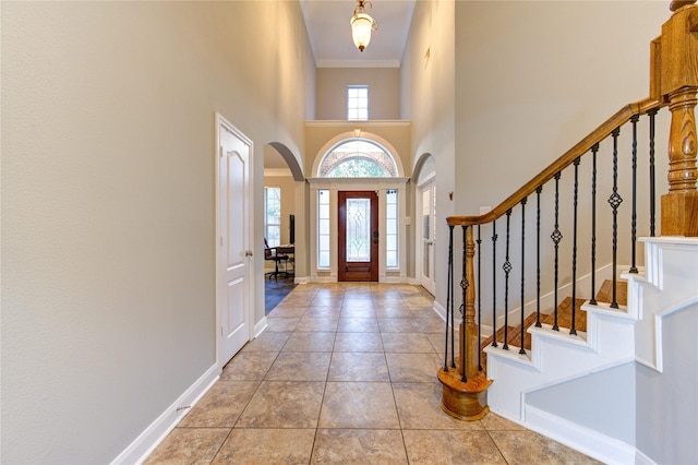 foyer with light tile patterned floors, ornamental molding, and a towering ceiling