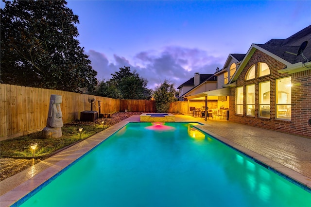 pool at dusk with an in ground hot tub and a patio