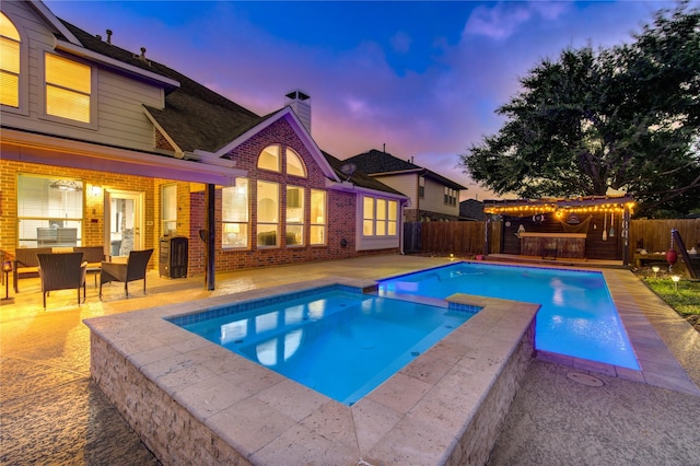 pool at dusk with an in ground hot tub, a patio, and an outdoor bar