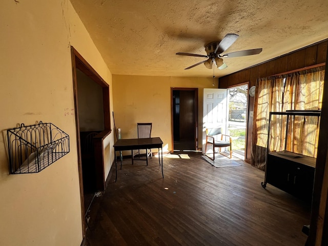 interior space with wooden walls, a textured ceiling, dark hardwood / wood-style floors, and ceiling fan