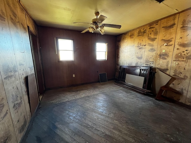 empty room with ceiling fan, dark hardwood / wood-style flooring, and wood walls