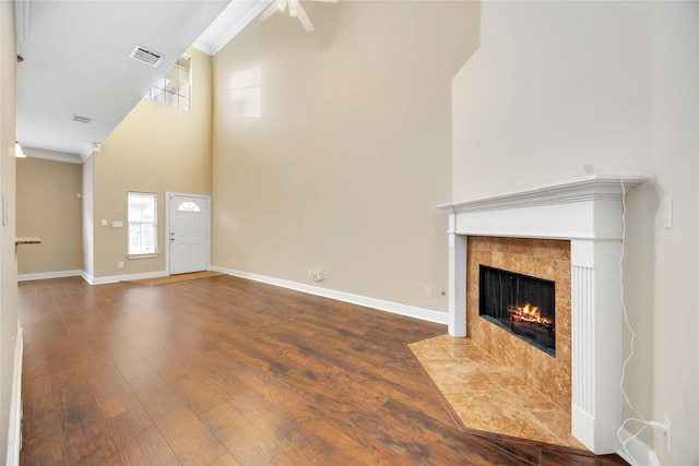 unfurnished living room featuring a towering ceiling, plenty of natural light, a fireplace, and hardwood / wood-style floors