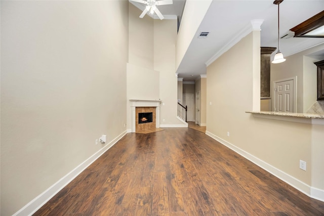 unfurnished living room featuring crown molding, dark hardwood / wood-style floors, ceiling fan, and a towering ceiling